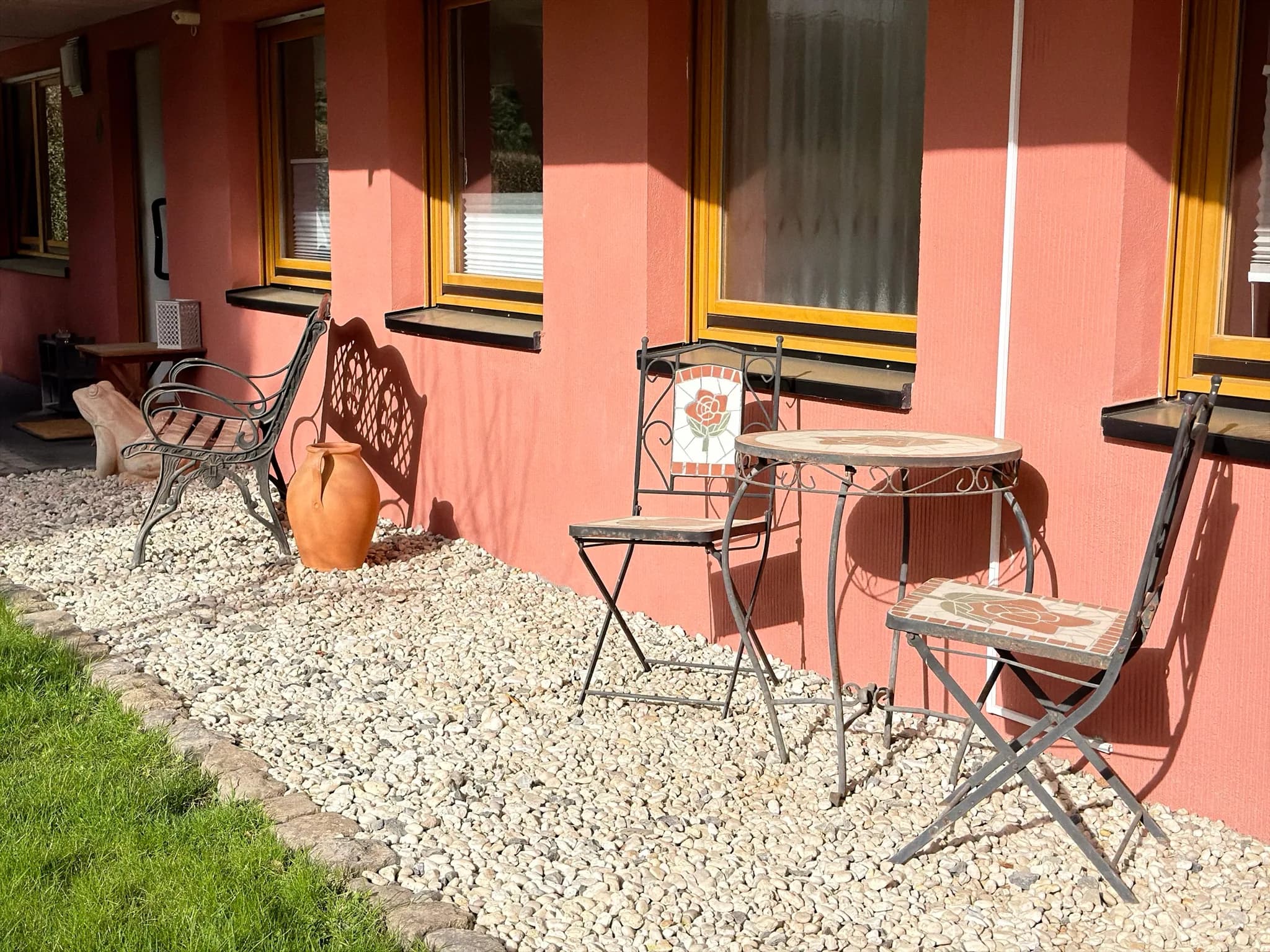 Terrasse mit Bistro-Set und Gartenbank im Sonnenlicht.